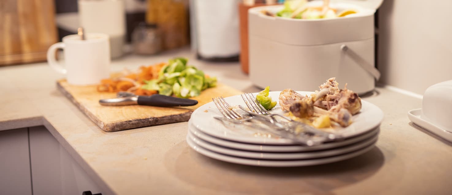 A stack of white plates with some leftover food next to a food waste caddy