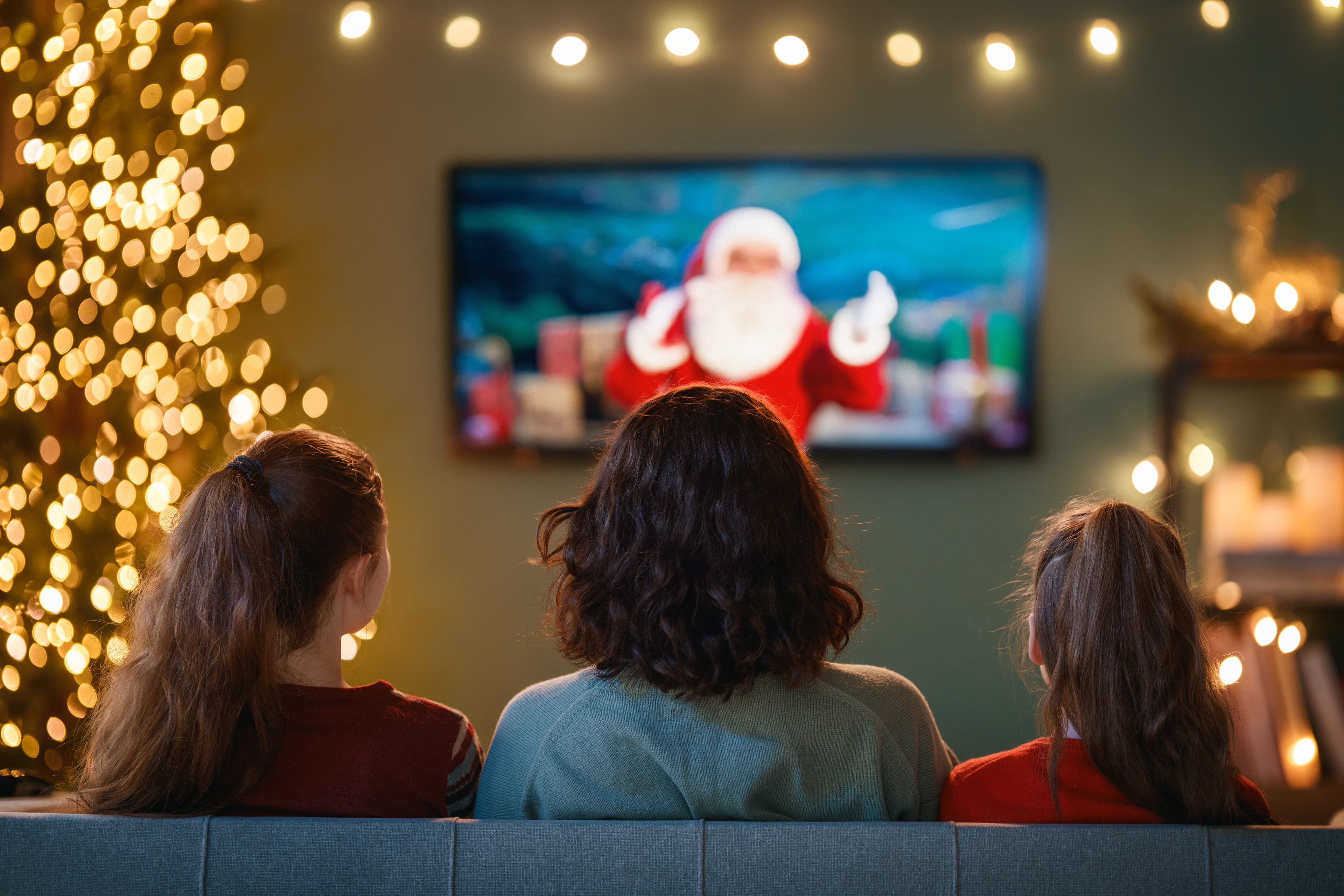 A rear view of a family consisting of two parents and two children sitting on a sofa watching television.