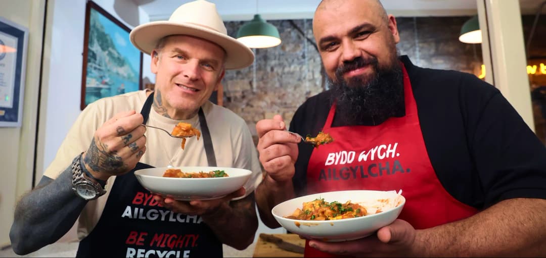 Matt Pritchard and Chris Roberts standing in Cardiff Market holding white bowls of food and forks.