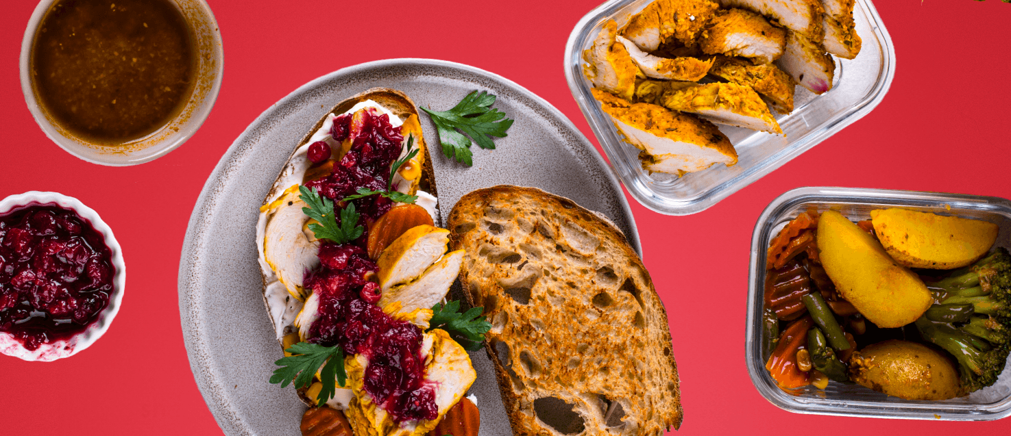 a table with an open turkey sandwich with cranberry sauce and other toppings, tubs of leftover veggies and leftover meat with pots of sauce and gravy