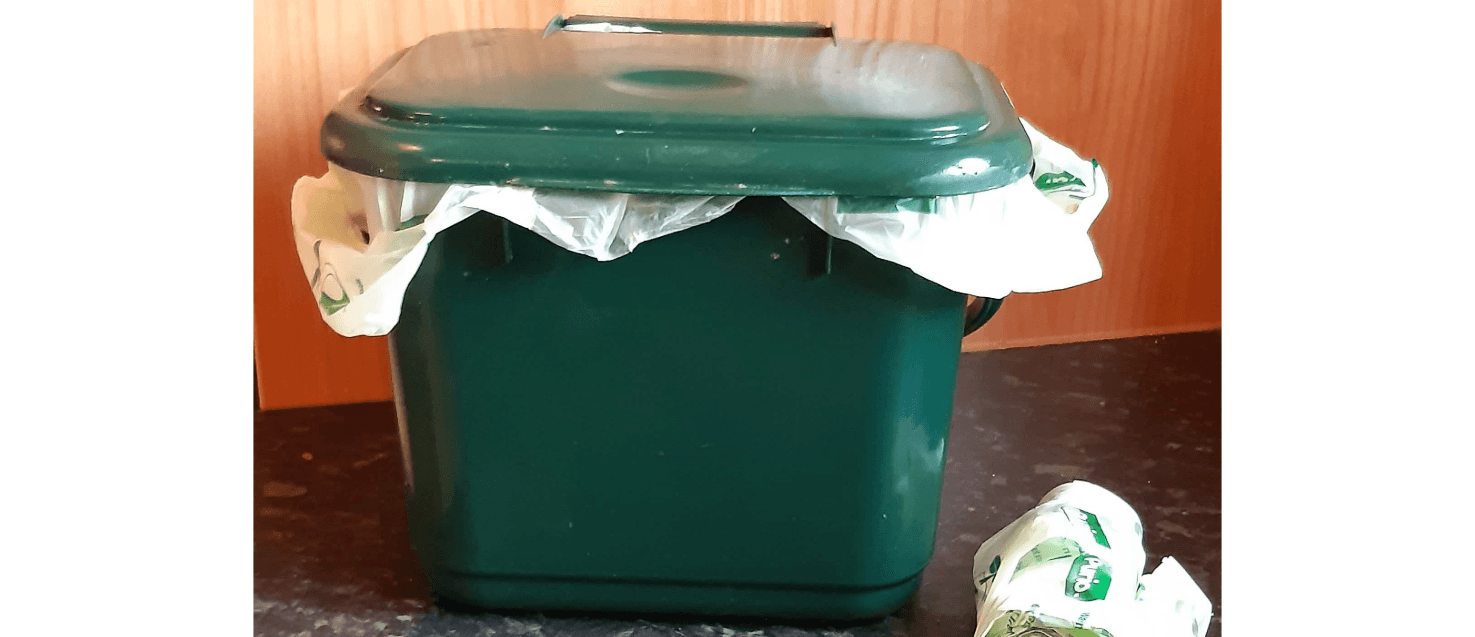 Green closed food caddy on a kitchen counter with a roll of green caddy liners to its left.
