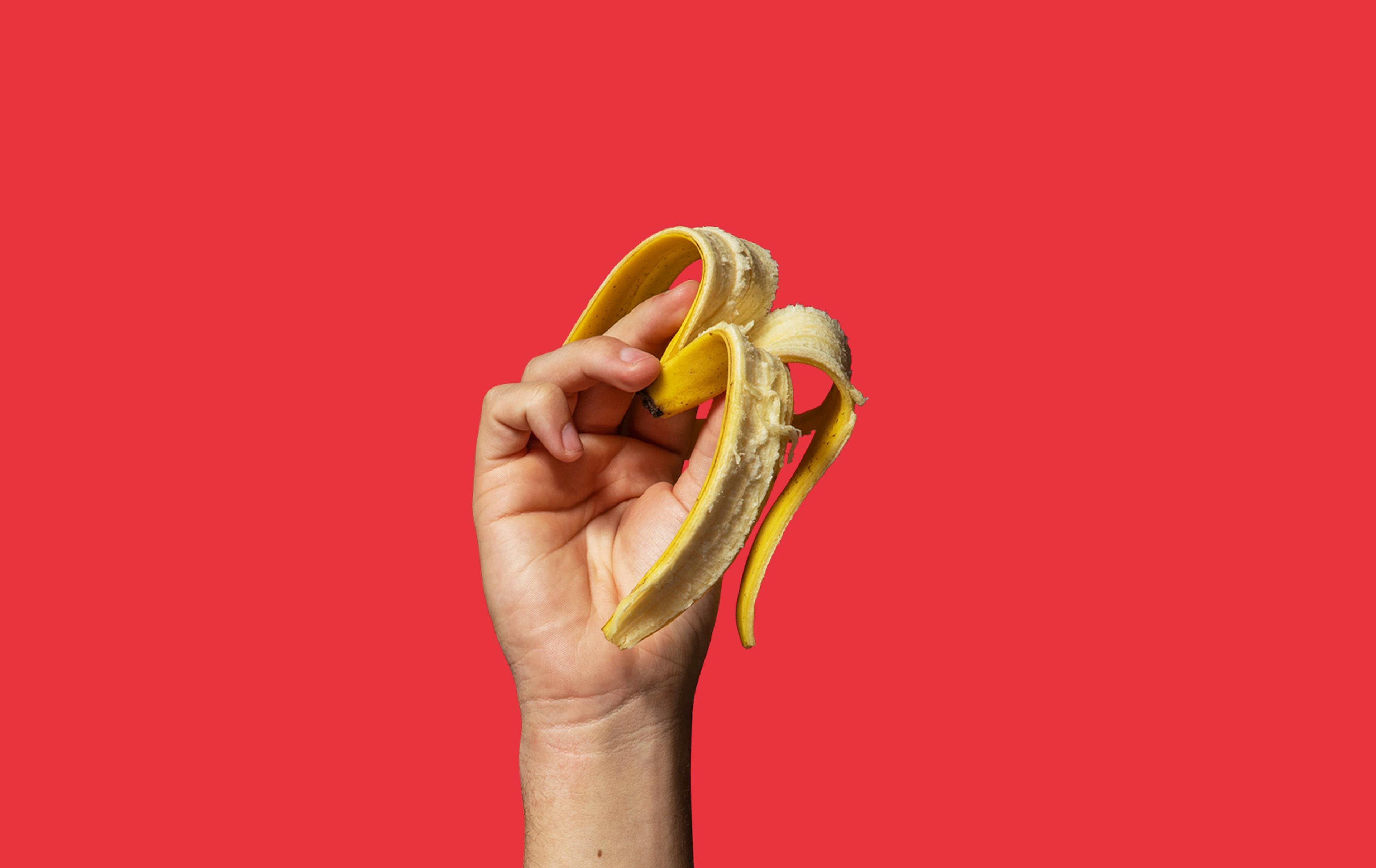 Hand holding a banana skin on a red background