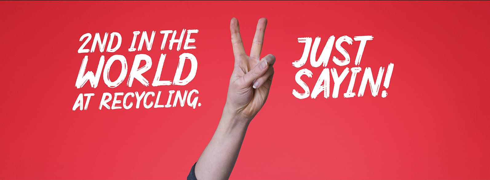 A red banner with a white person's hand holding up two fingers in a peace sign. Text reads: 2nd in the world at recycling. Just sayin!