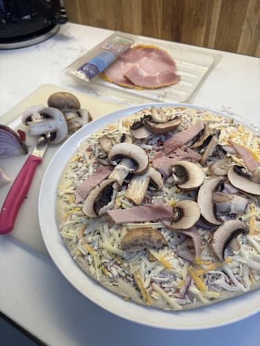 A frozen pizza with added toppings of ham and mushroom added from leftover food.