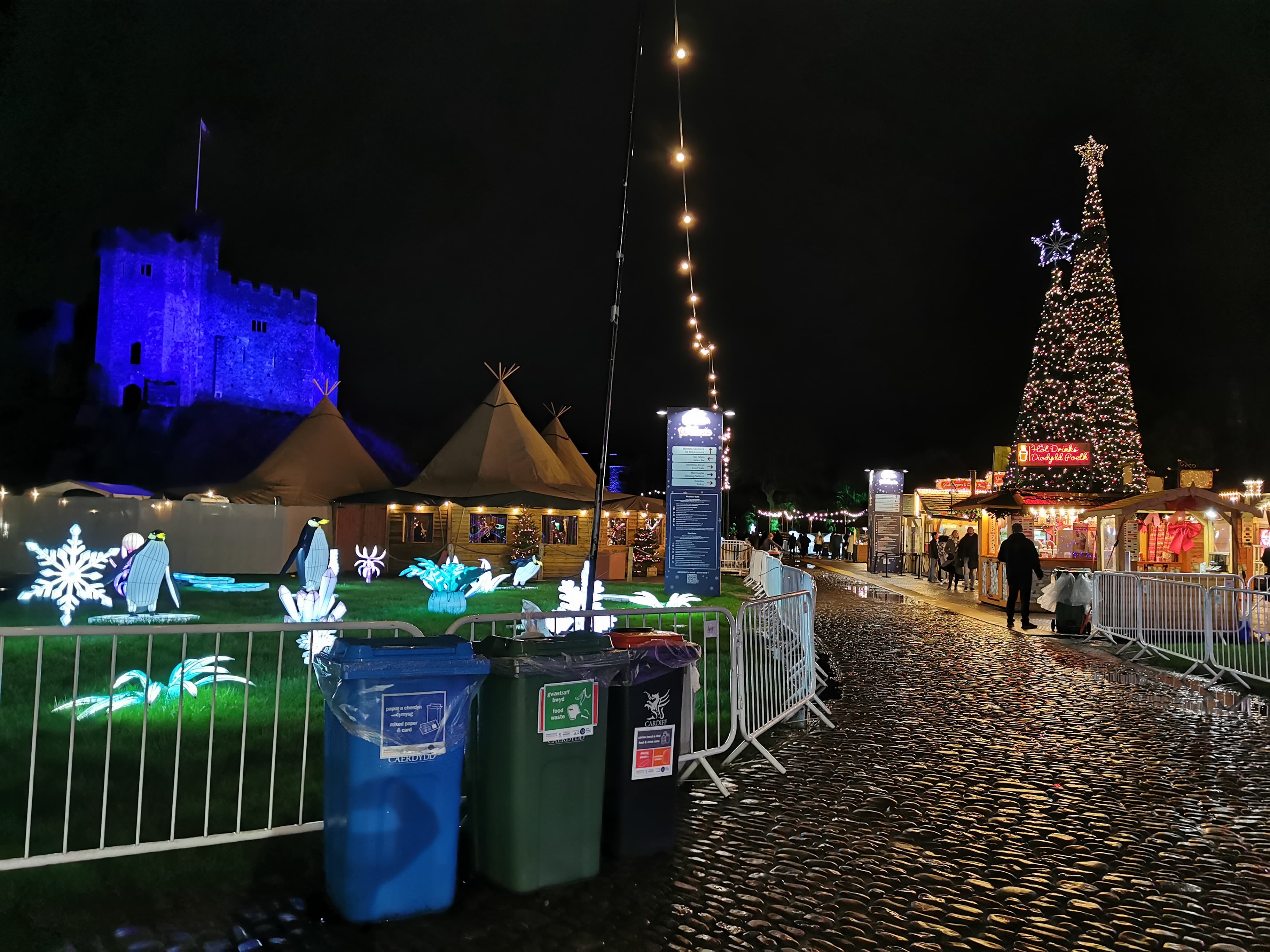 Three differently coloured recycling bins in front of Christmas decorations and a castle keep