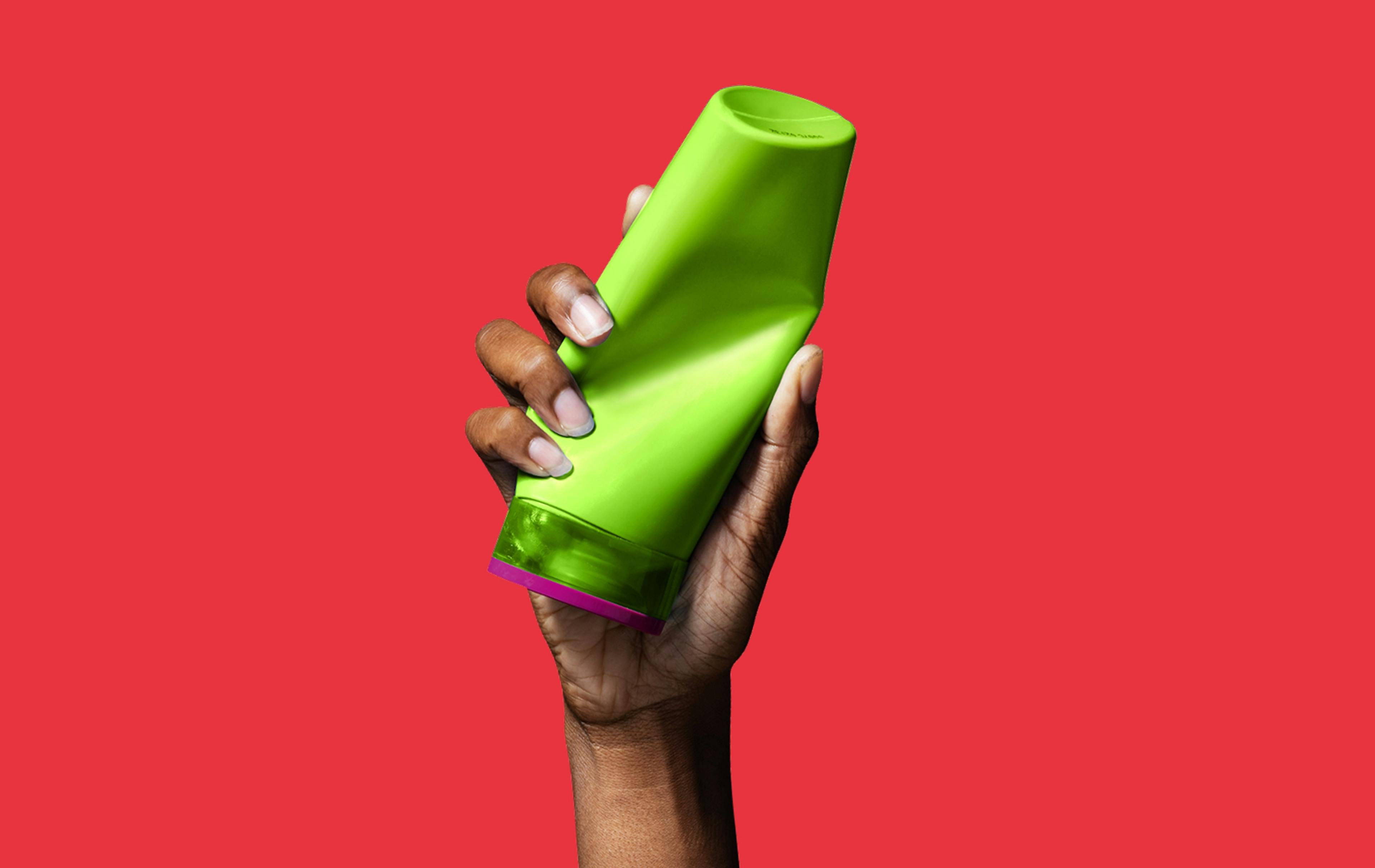 Hand crushing green plastic shampoo bottle on a red background